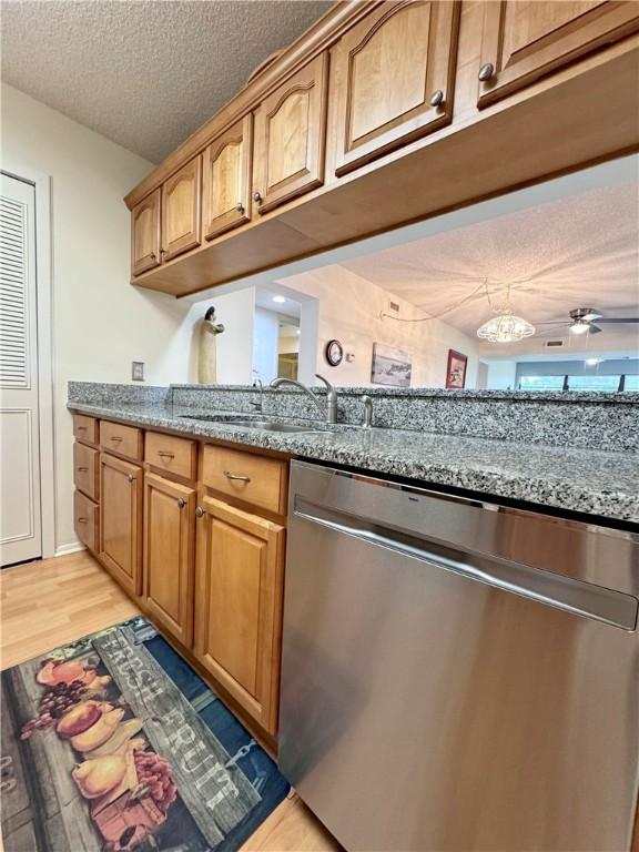 kitchen featuring dishwasher, light stone counters, light wood-type flooring, and a textured ceiling