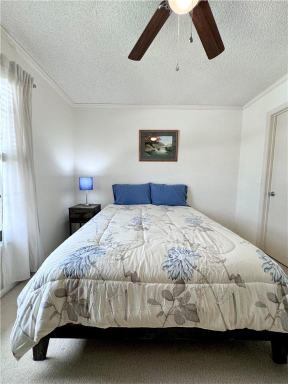 bedroom with ceiling fan, carpet floors, a textured ceiling, and ornamental molding