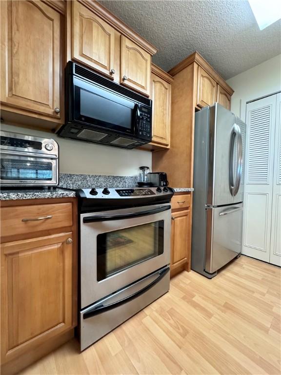 kitchen featuring a skylight, dark stone counters, light hardwood / wood-style floors, a textured ceiling, and appliances with stainless steel finishes