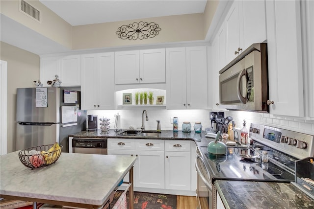 kitchen featuring sink, appliances with stainless steel finishes, white cabinets, decorative backsplash, and dark stone counters