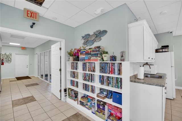 hallway with a drop ceiling, light tile patterned floors, and sink