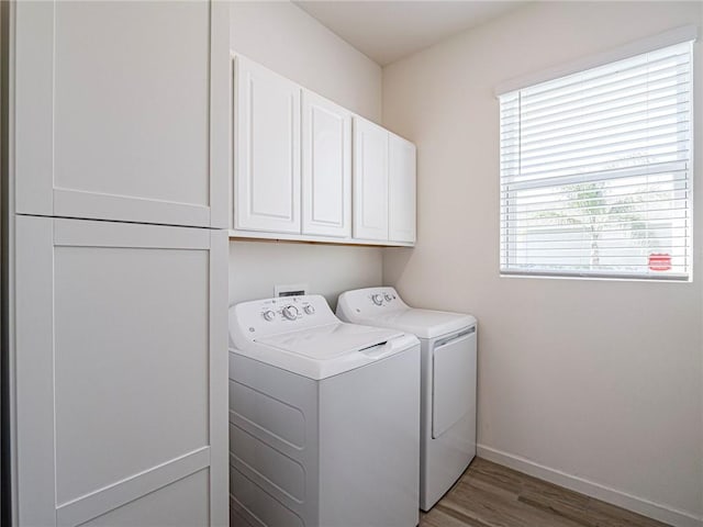 washroom featuring washing machine and clothes dryer, cabinet space, baseboards, and wood finished floors