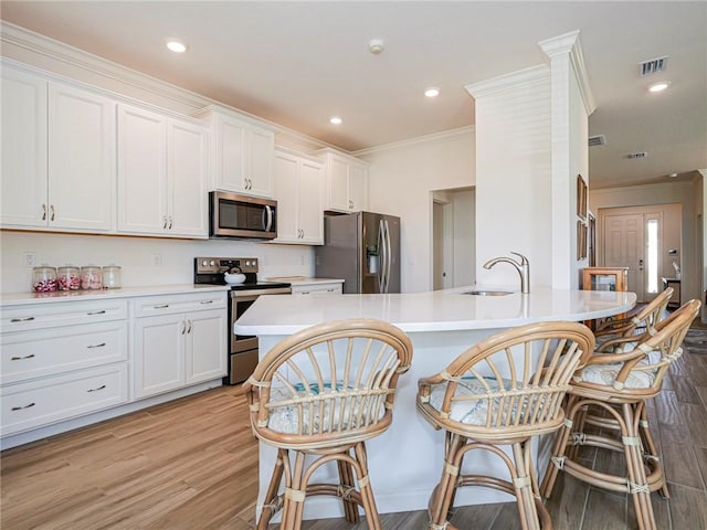 kitchen with light wood finished floors, a sink, a kitchen breakfast bar, stainless steel appliances, and light countertops