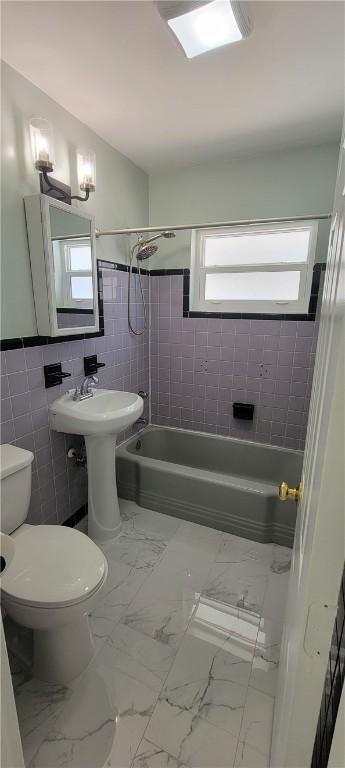 bathroom featuring toilet, shower / washtub combination, and tile walls