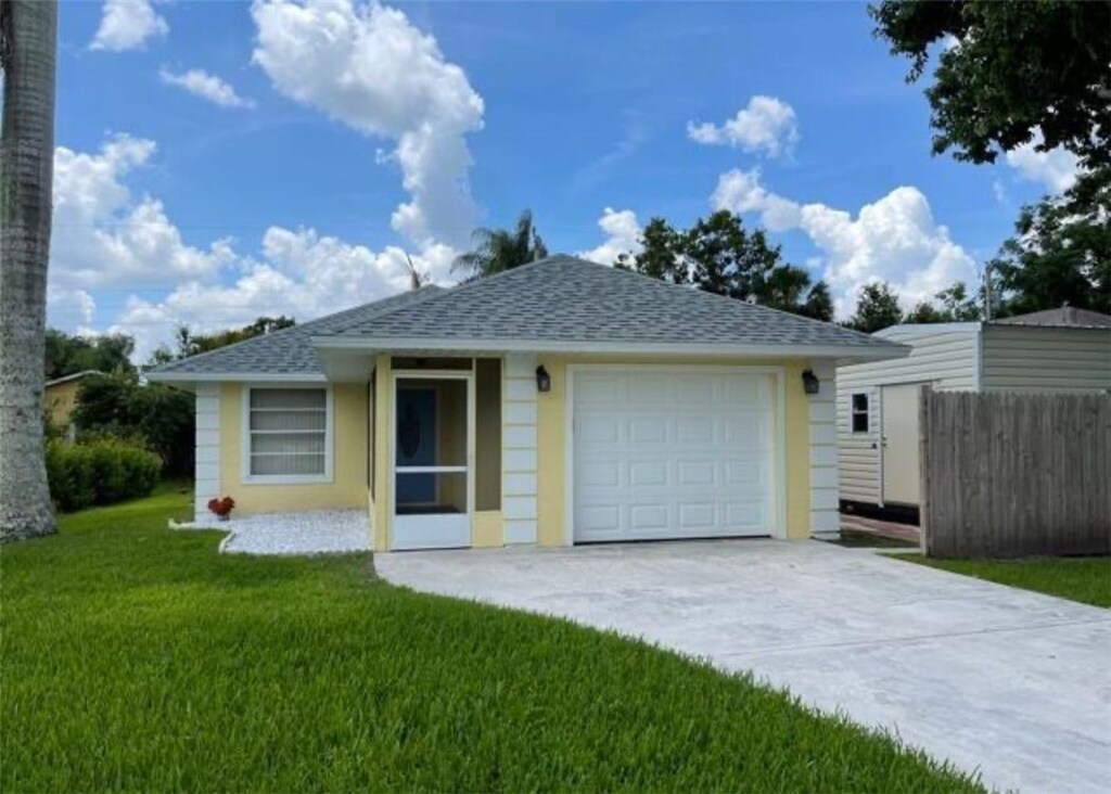 2825 1st Pl, Vero Beach, FL 32968 - view of front facade featuring driveway, a garage, fence, a front lawn, and a shingled roof