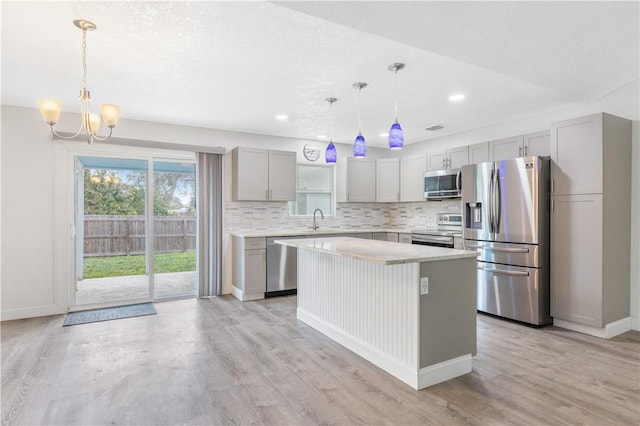 kitchen with appliances with stainless steel finishes, a center island, pendant lighting, and light hardwood / wood-style flooring