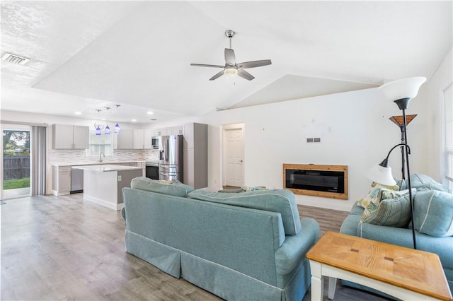 living room with lofted ceiling, sink, light hardwood / wood-style floors, and ceiling fan