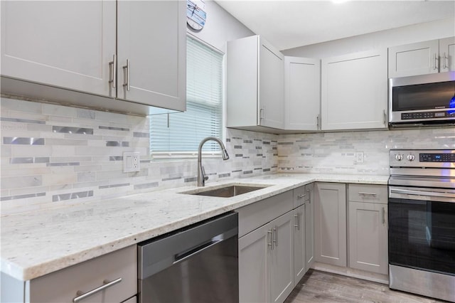 kitchen with light stone counters, sink, backsplash, and appliances with stainless steel finishes