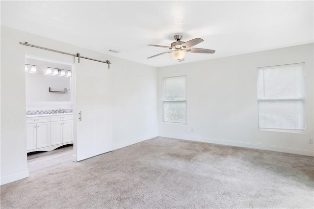 spare room with light carpet, sink, a barn door, and ceiling fan