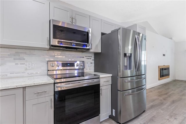 kitchen with tasteful backsplash, light stone counters, gray cabinets, and appliances with stainless steel finishes