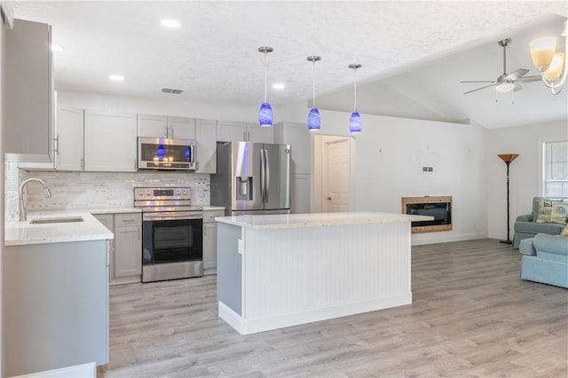 kitchen with a kitchen island, appliances with stainless steel finishes, decorative light fixtures, lofted ceiling, and sink