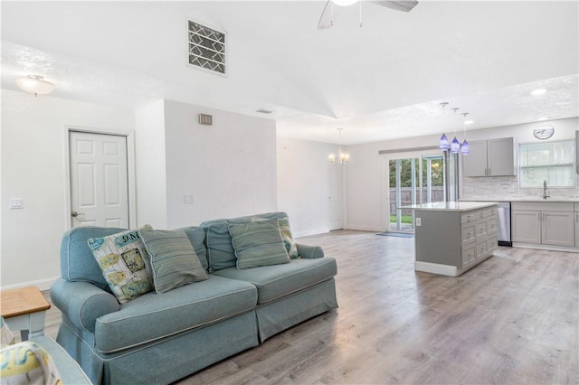 living room featuring vaulted ceiling, sink, ceiling fan with notable chandelier, and light wood-type flooring