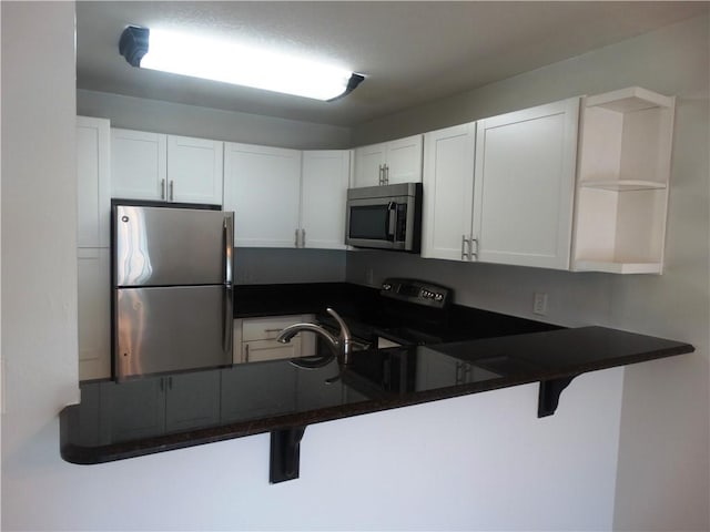 kitchen with open shelves, dark countertops, a kitchen breakfast bar, stainless steel appliances, and white cabinetry