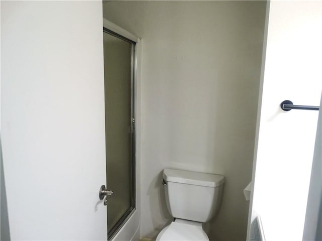 bathroom featuring toilet and shower / bath combination with glass door
