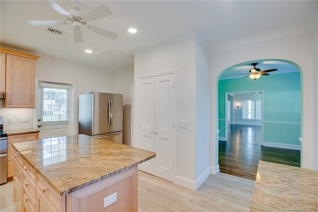 kitchen featuring light stone countertops, light wood-type flooring, stainless steel appliances, light brown cabinets, and a kitchen island