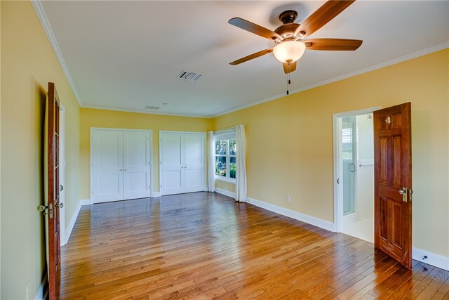 unfurnished bedroom featuring light hardwood / wood-style floors, multiple closets, crown molding, and ceiling fan