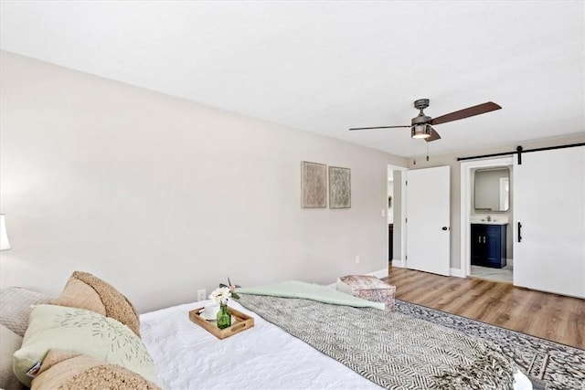 bedroom featuring sink, hardwood / wood-style flooring, ceiling fan, ensuite bathroom, and a barn door