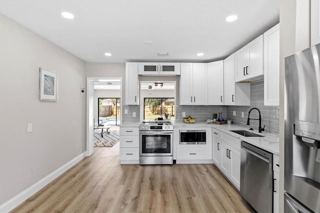 kitchen with sink, light wood-type flooring, appliances with stainless steel finishes, white cabinets, and backsplash