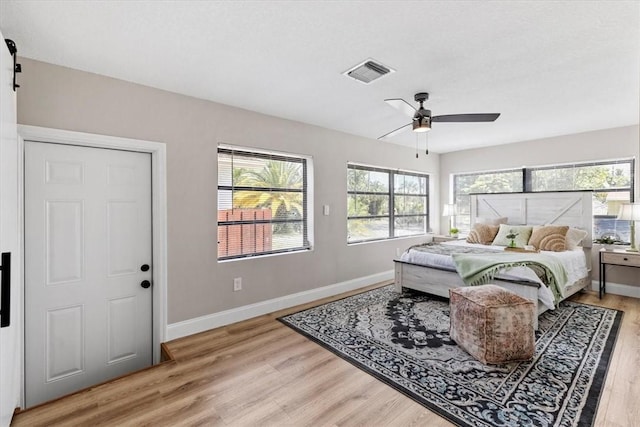 bedroom with ceiling fan, a barn door, and light wood-type flooring