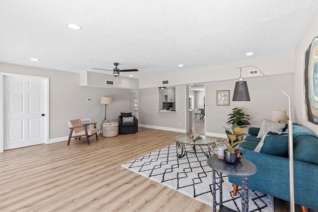 living room with ceiling fan, a textured ceiling, and light hardwood / wood-style flooring