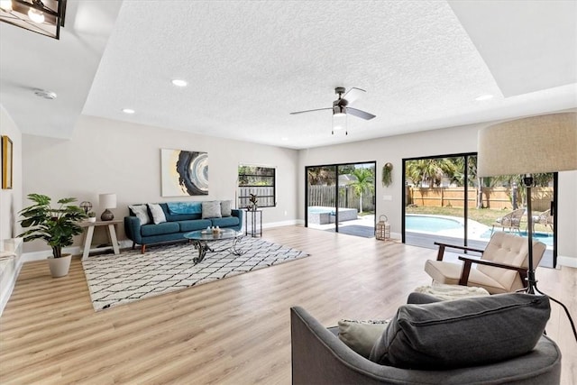 living room featuring ceiling fan, light hardwood / wood-style flooring, and a textured ceiling