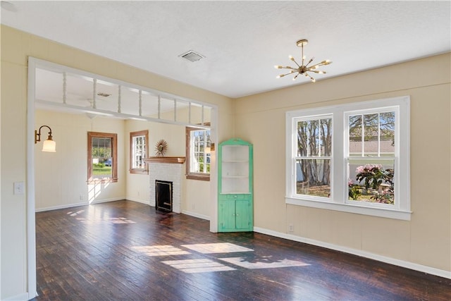 unfurnished living room featuring a fireplace, dark wood-type flooring, a wealth of natural light, and a chandelier