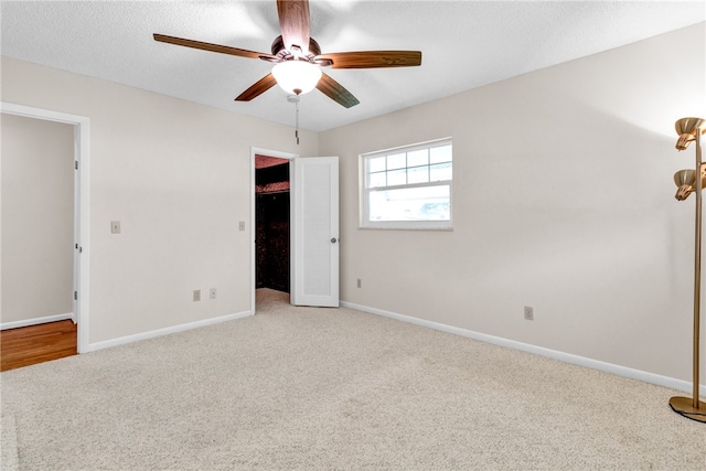 unfurnished bedroom with a textured ceiling, a spacious closet, light carpet, and ceiling fan