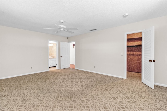 unfurnished bedroom featuring a closet, a spacious closet, a textured ceiling, ceiling fan, and ensuite bathroom