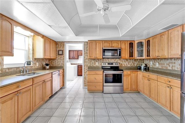 kitchen with sink, appliances with stainless steel finishes, ceiling fan, washer / dryer, and a raised ceiling