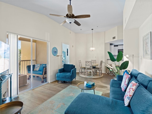 living room with baseboards, wood finished floors, a towering ceiling, and ceiling fan with notable chandelier