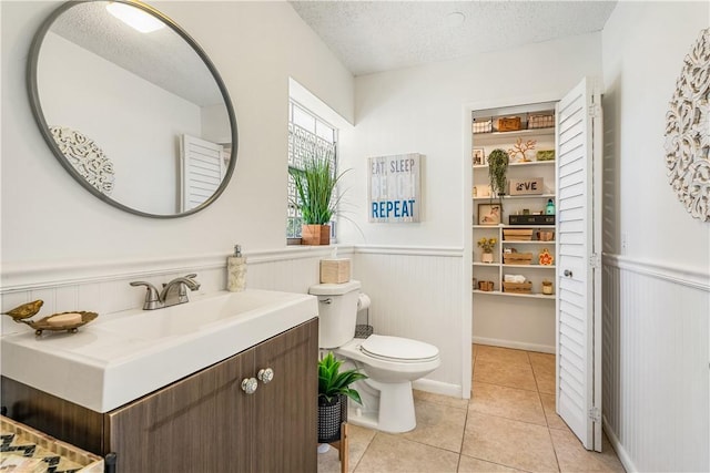 bathroom featuring a textured ceiling, toilet, a wainscoted wall, and tile patterned floors