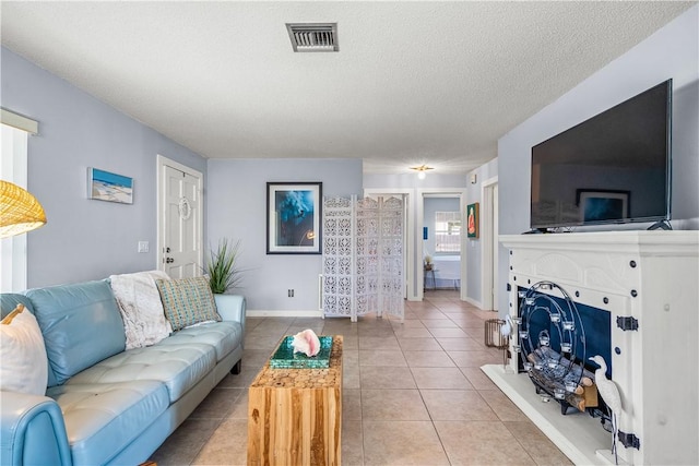 living room with a textured ceiling, visible vents, baseboards, and light tile patterned floors