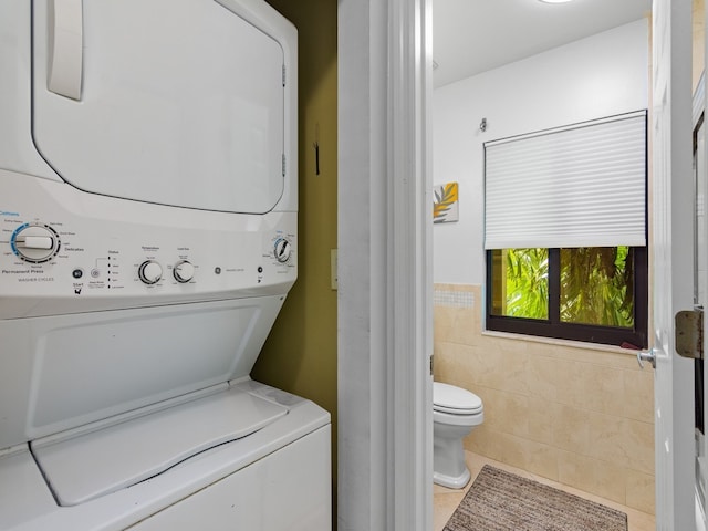 clothes washing area with tile patterned flooring, stacked washer / dryer, and tile walls