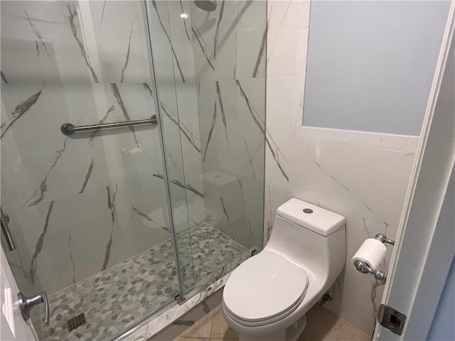 bathroom featuring a shower with door, tile walls, and toilet