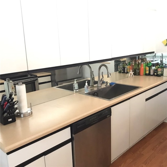 kitchen with stainless steel dishwasher, sink, hardwood / wood-style flooring, and white cabinets