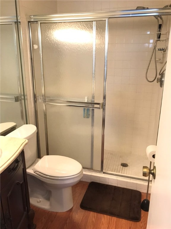 bathroom with walk in shower, hardwood / wood-style floors, vanity, and toilet