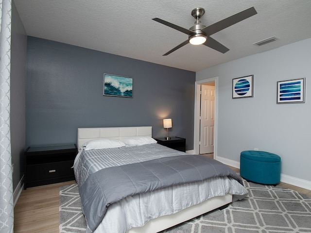 bedroom featuring a textured ceiling, wood finished floors, visible vents, and baseboards