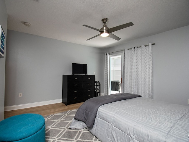 bedroom with ceiling fan, a textured ceiling, baseboards, and wood finished floors