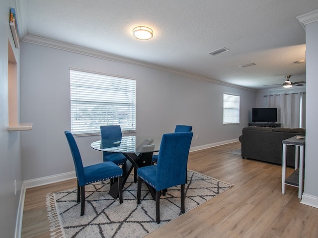 dining space featuring visible vents, a textured ceiling, ornamental molding, and wood finished floors