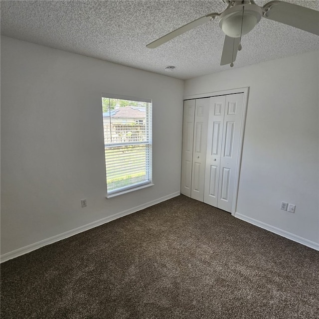 unfurnished bedroom with ceiling fan, dark carpet, a textured ceiling, and a closet