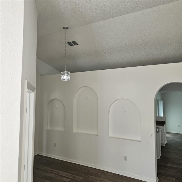 empty room with a chandelier, a textured ceiling, vaulted ceiling, and dark wood-type flooring