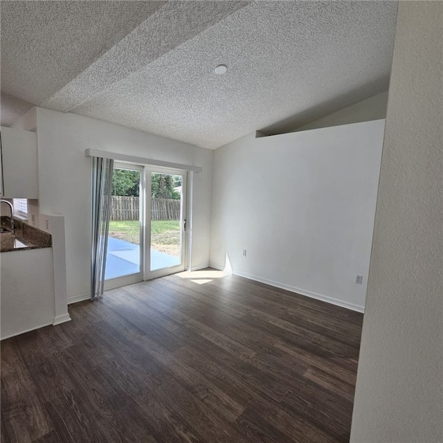 empty room with a textured ceiling, vaulted ceiling, dark wood-type flooring, and sink