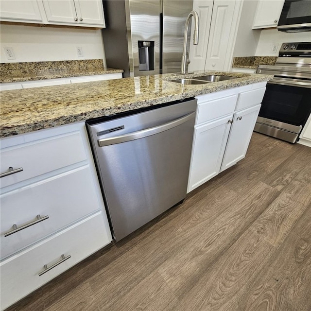 kitchen with sink, dark wood-type flooring, stainless steel appliances, light stone counters, and white cabinets