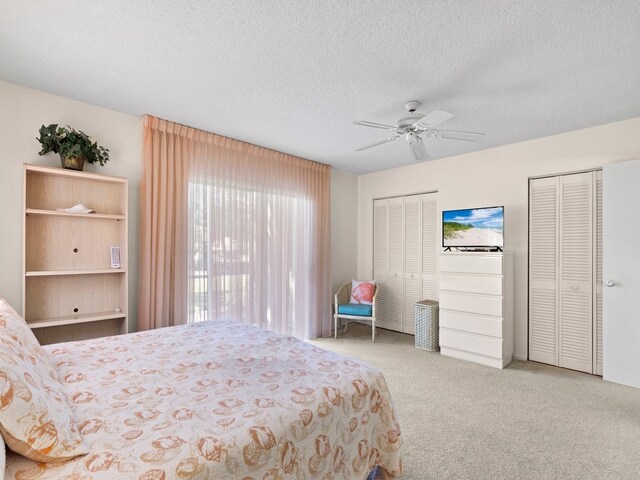 bedroom with a textured ceiling, light colored carpet, ceiling fan, and two closets