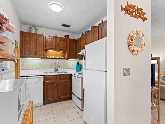 kitchen with white appliances, sink, light tile patterned floors, and a textured ceiling