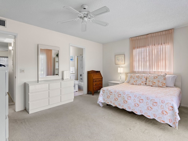 bedroom featuring a textured ceiling, ensuite bath, light carpet, and ceiling fan