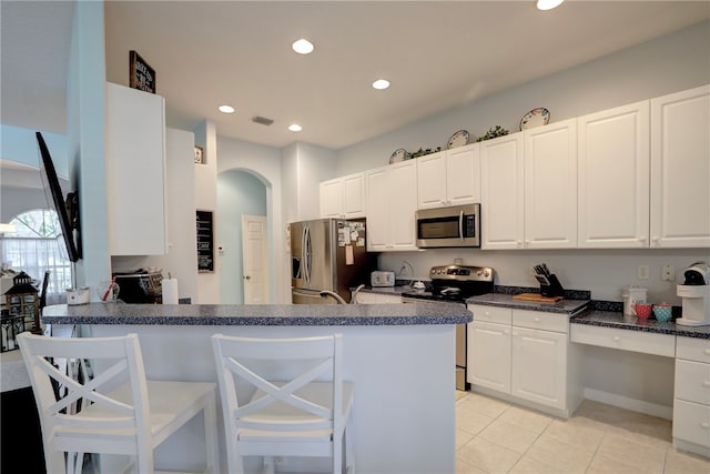 kitchen with white cabinets, kitchen peninsula, light tile patterned floors, a breakfast bar, and appliances with stainless steel finishes