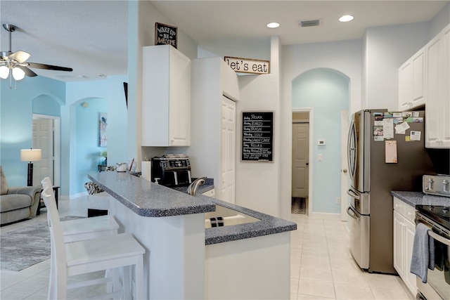 kitchen with light tile patterned flooring, stainless steel appliances, white cabinets, a breakfast bar area, and kitchen peninsula