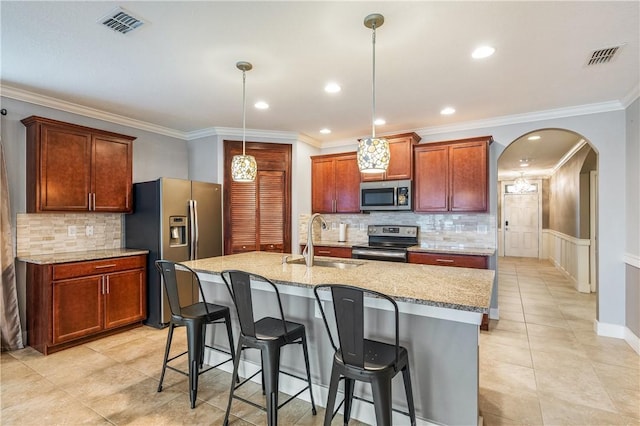 kitchen featuring a center island with sink, stainless steel appliances, light stone countertops, pendant lighting, and sink