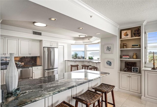 kitchen featuring a kitchen bar, stainless steel appliances, a healthy amount of sunlight, and dark stone countertops